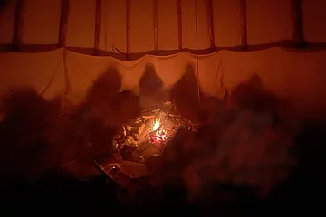 Blick ins Tipi bei Nacht, in dem ein kleines Lagerfeuer brennt